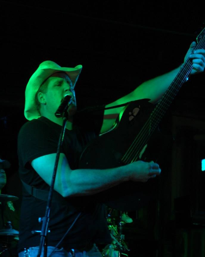 Scott DuBose singing and playing guitar on stage in a cowboy hat