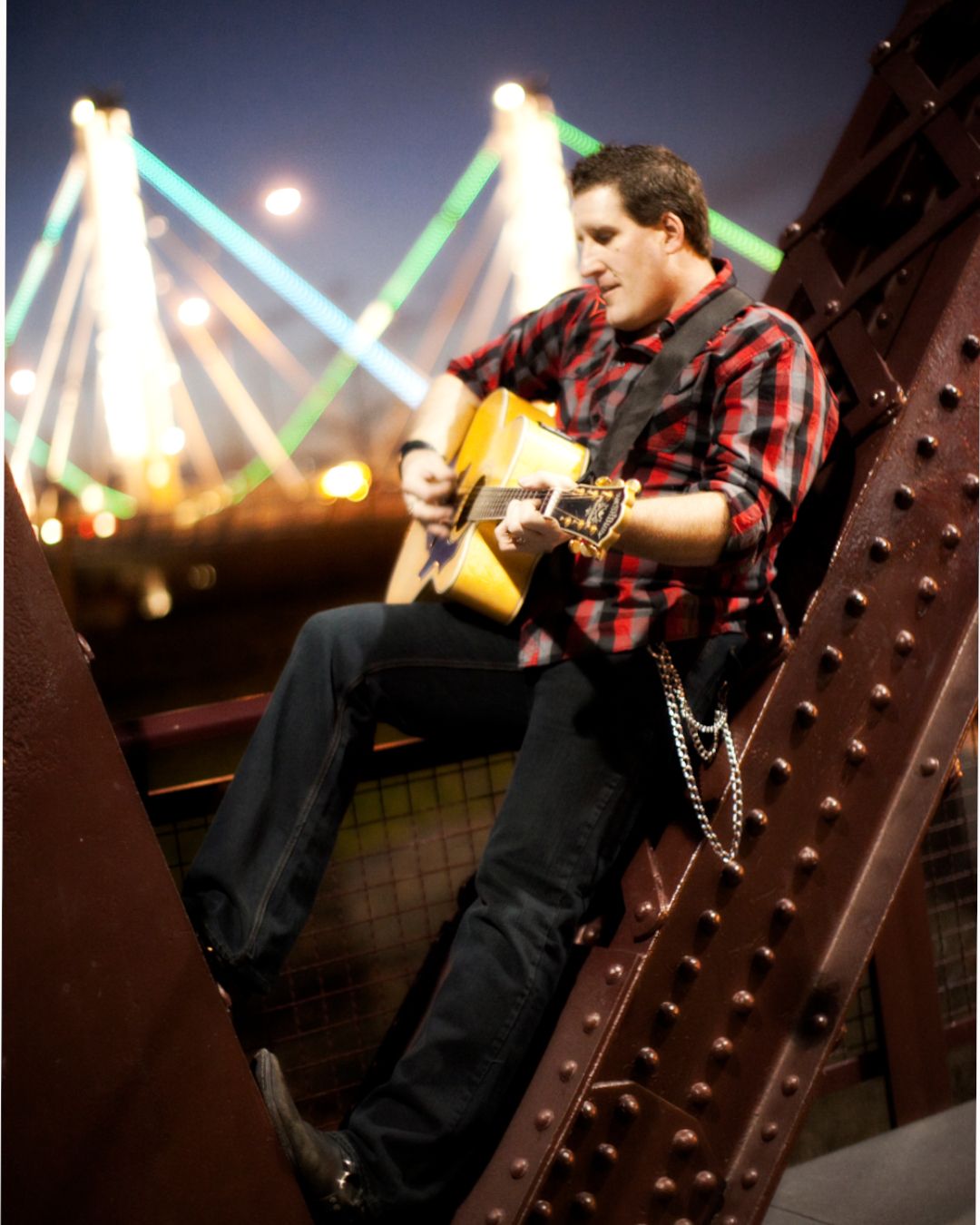 Scott DuBose playing acoustic guitar on a Chicago bridge at night